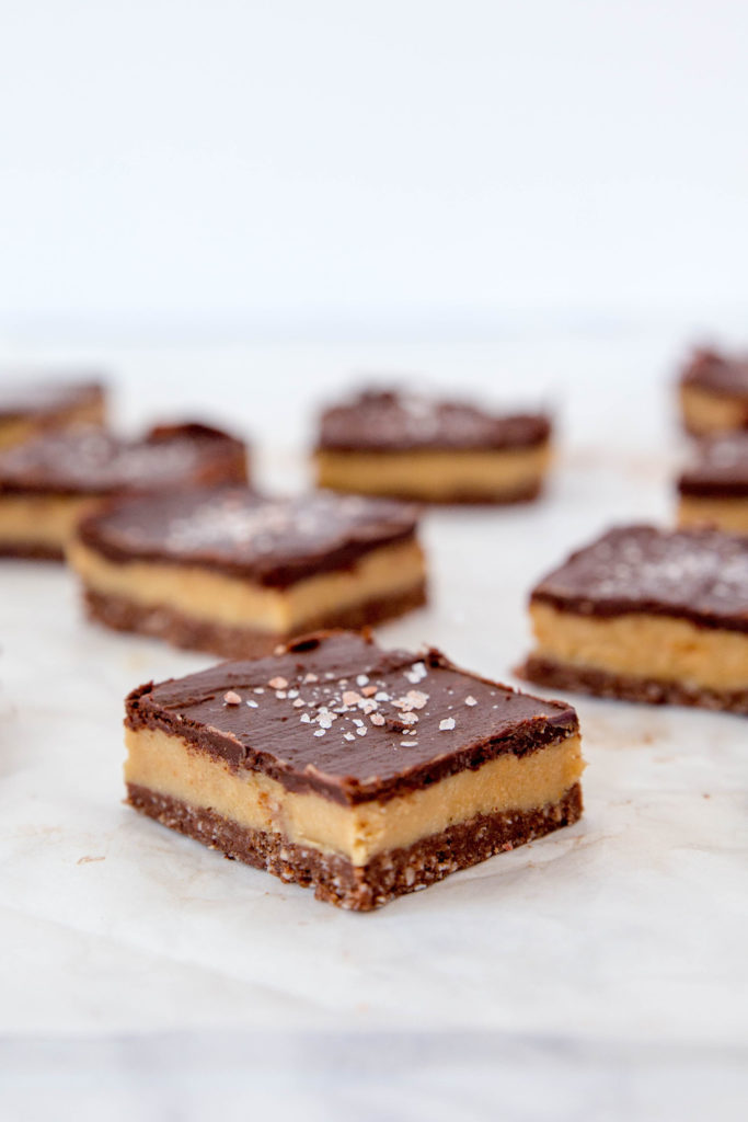 Caramel slice with dark chocolate sitting on parchment paper