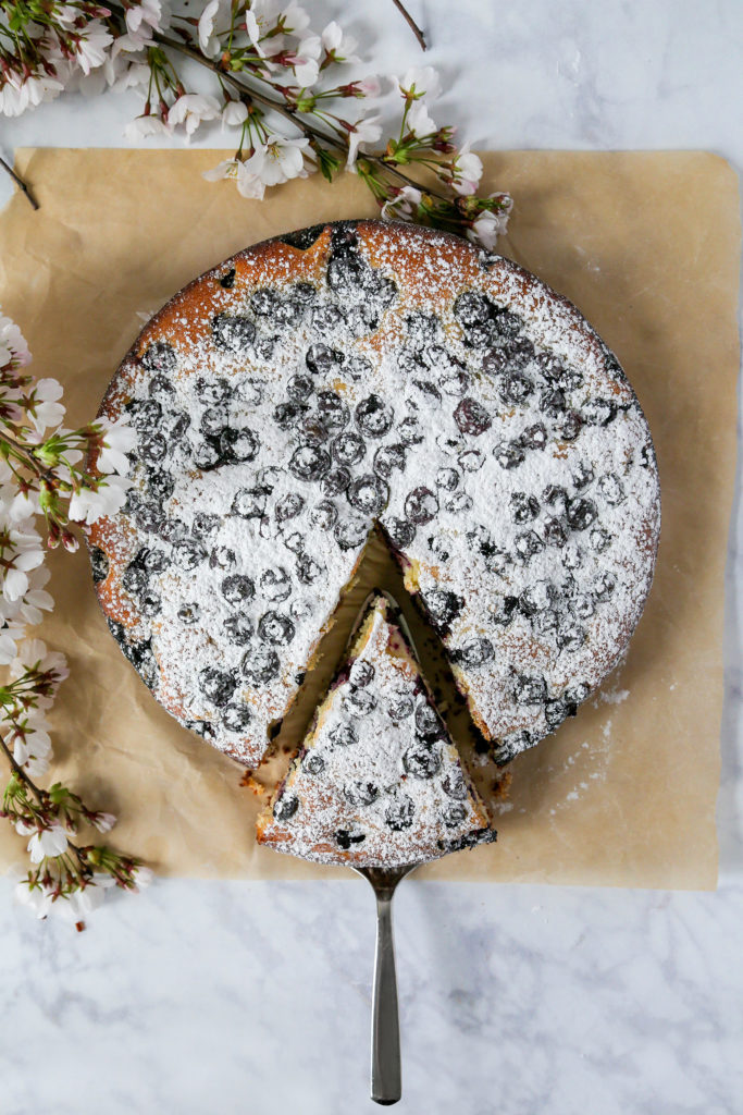 Blueberry lemon cake sitting on brown parchment paper with a cake serving tool