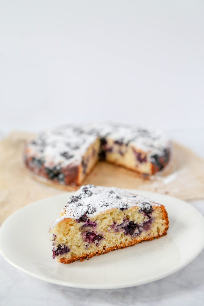 A slice of blueberry lemon cake sitting on a white plate