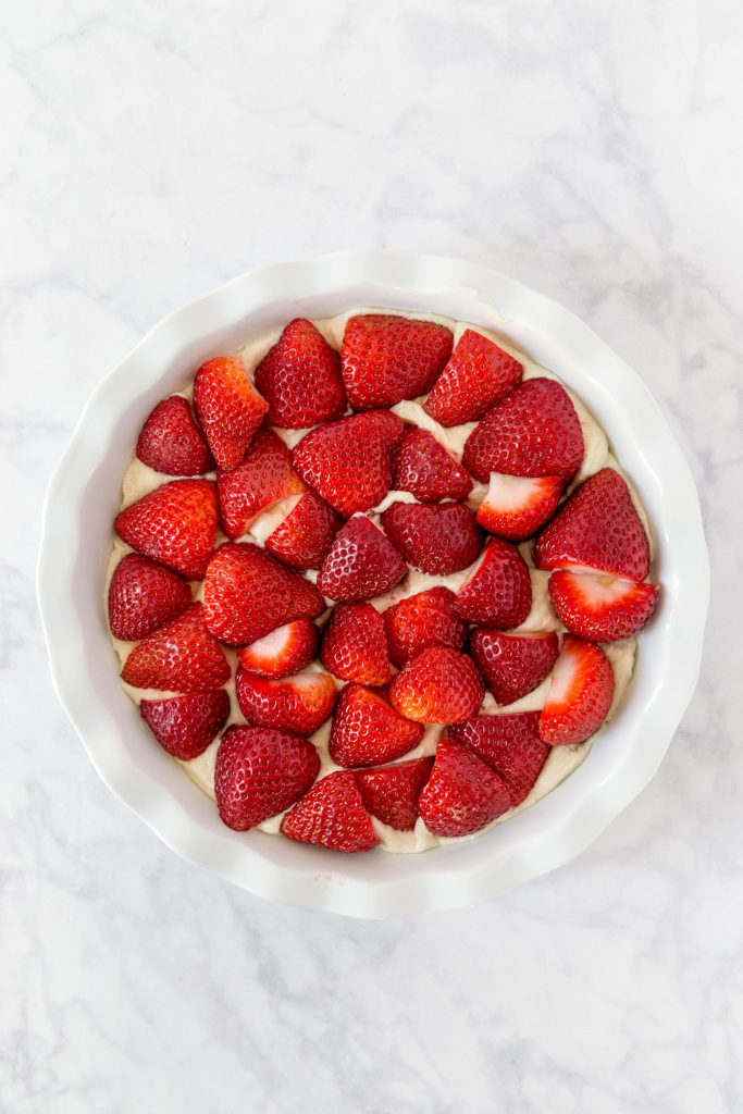 A white pie plate filled with cake batter and fresh strawberries, set on a grey marbled background