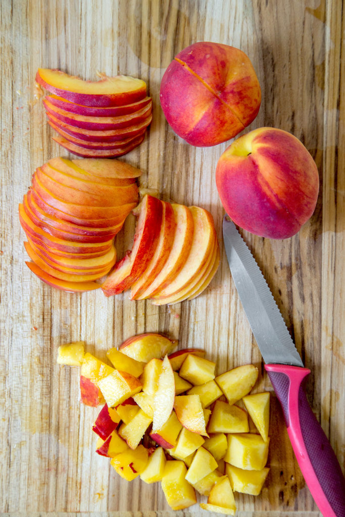 Sliced peaches and cubed peaches on a wooden cutting board with a knife