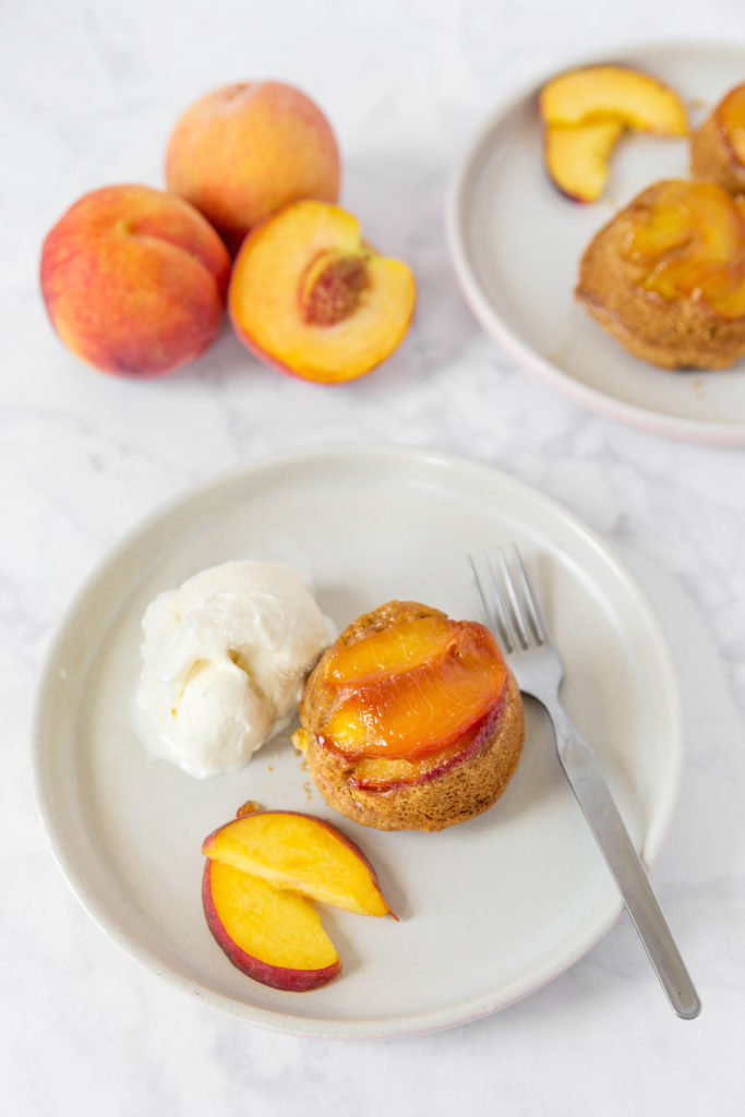 Peach cake and ice cream on a white plate with 3 peaches in the background