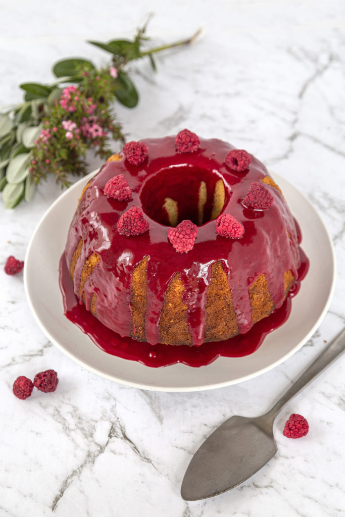 A bundt cake with raspberry glaze, sitting on a white plate. 