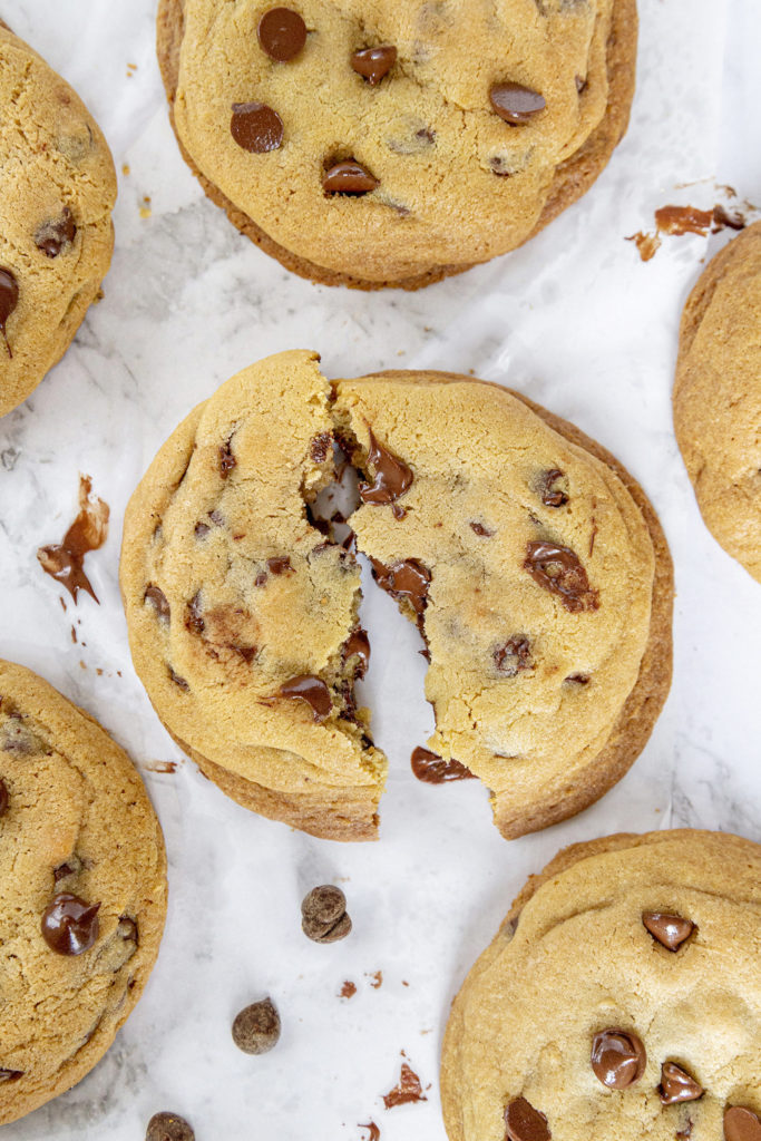 Chocolate chip cookies on a marble background. Middle cookie is broken in half to show oozing chocolate.