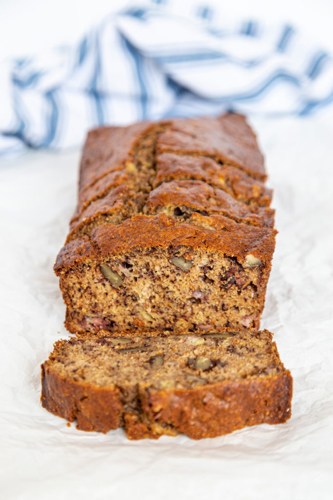 Front view of sliced banana bread with blue and white striped kitchen towel in the back