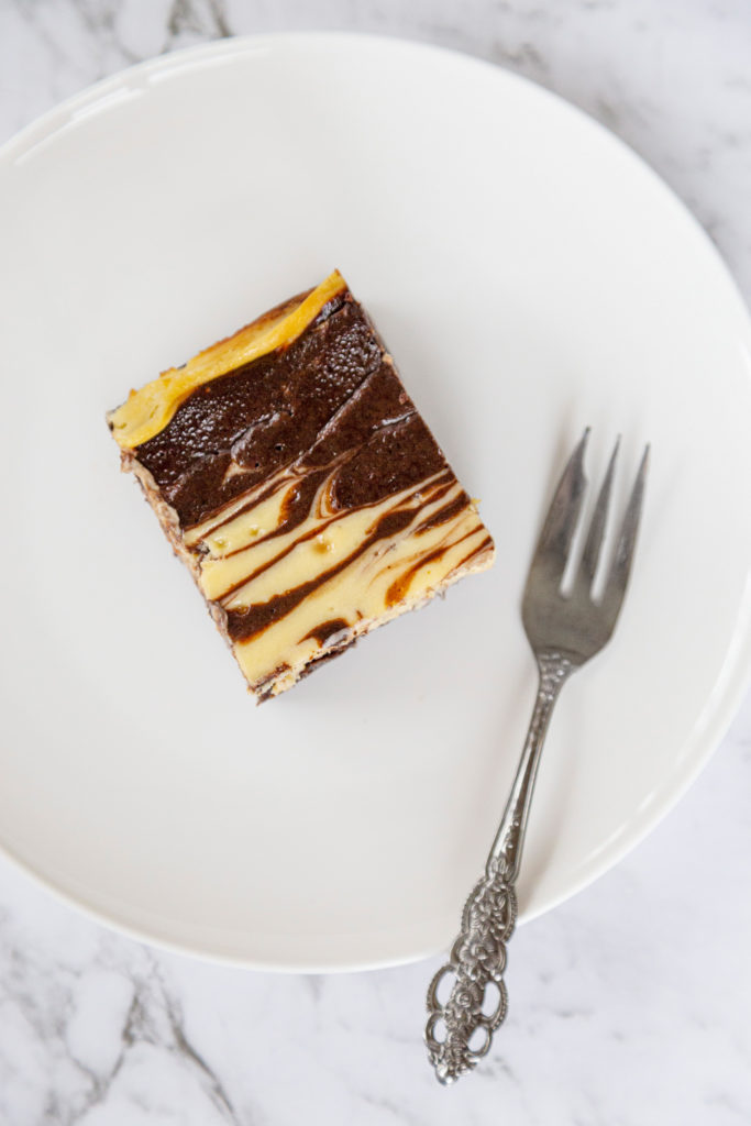 A cheesecake swirl brownie on a white plate with a cake fork