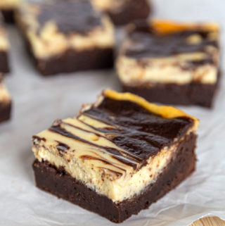Cheesecake swirl brownies sitting on parchment paper on top of a wooden cutting board