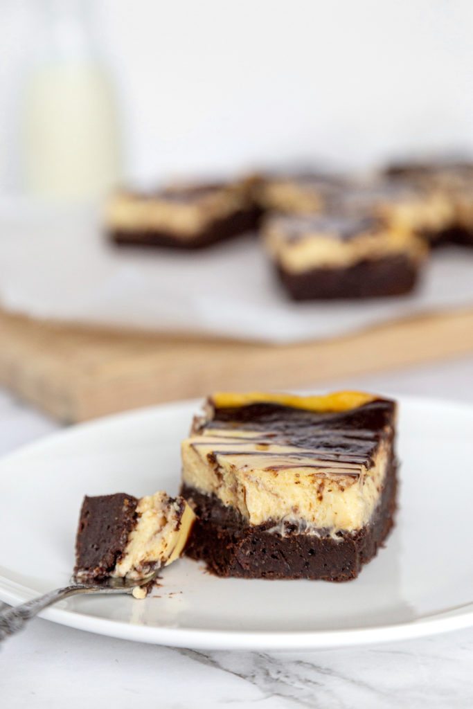 a cheesecake brownie on a white plate, with a fork