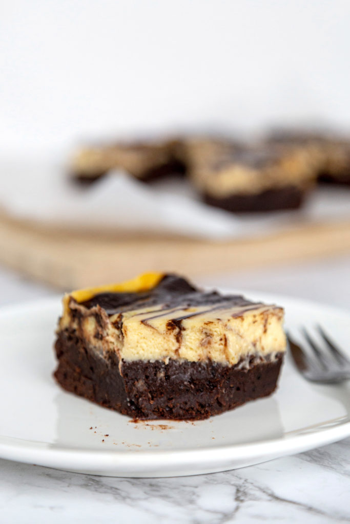 a cheesecake brownie on a white plate, with a fork