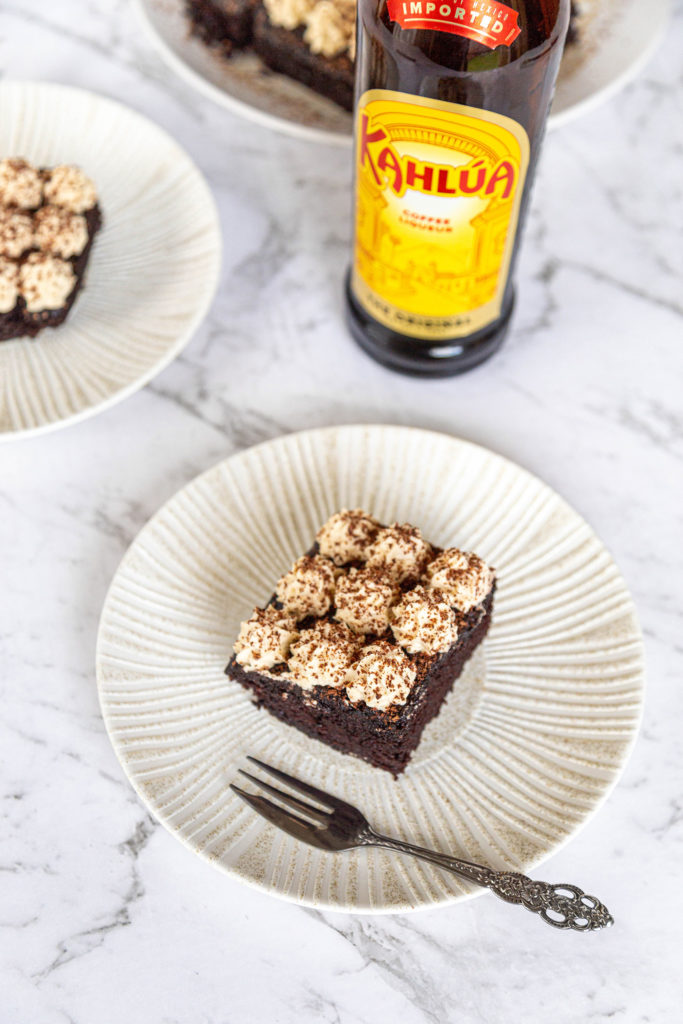 An overhead shot of a slice of kahlua chocolate cake on a cream plate with a small fork. A bottle of Kahlua behind the cake.