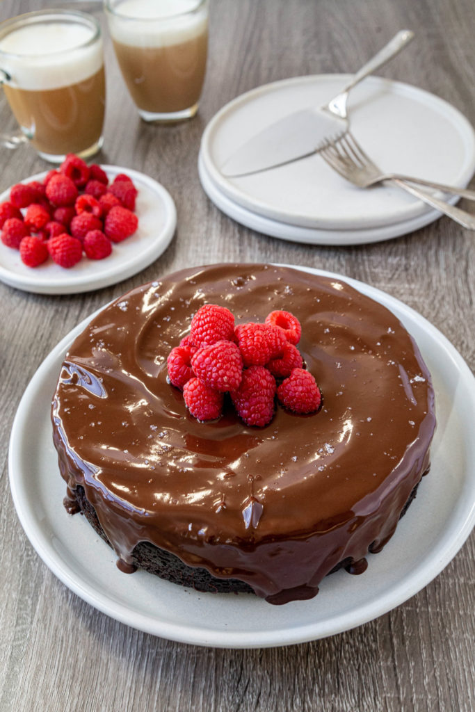 A whole chocolate cake sitting on a white plate with a pile of raspberries in the center of the cake