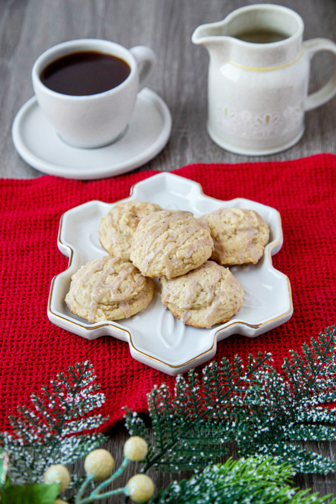 A white plate shaped like a snowflake with 5 cookies on it, sitting on a red kitchen towel. A cup of coffee sits behind the cookies, with a milk jug. 