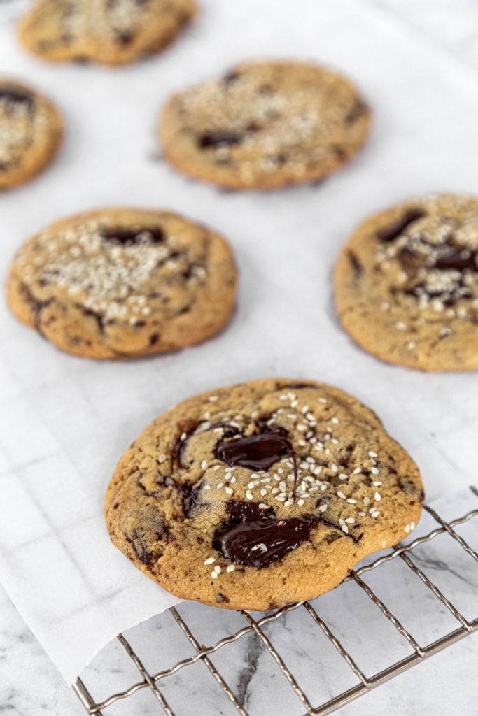 Tahini chocolate chunk cookies sitting on white parchment paper, on a wire cooling rack