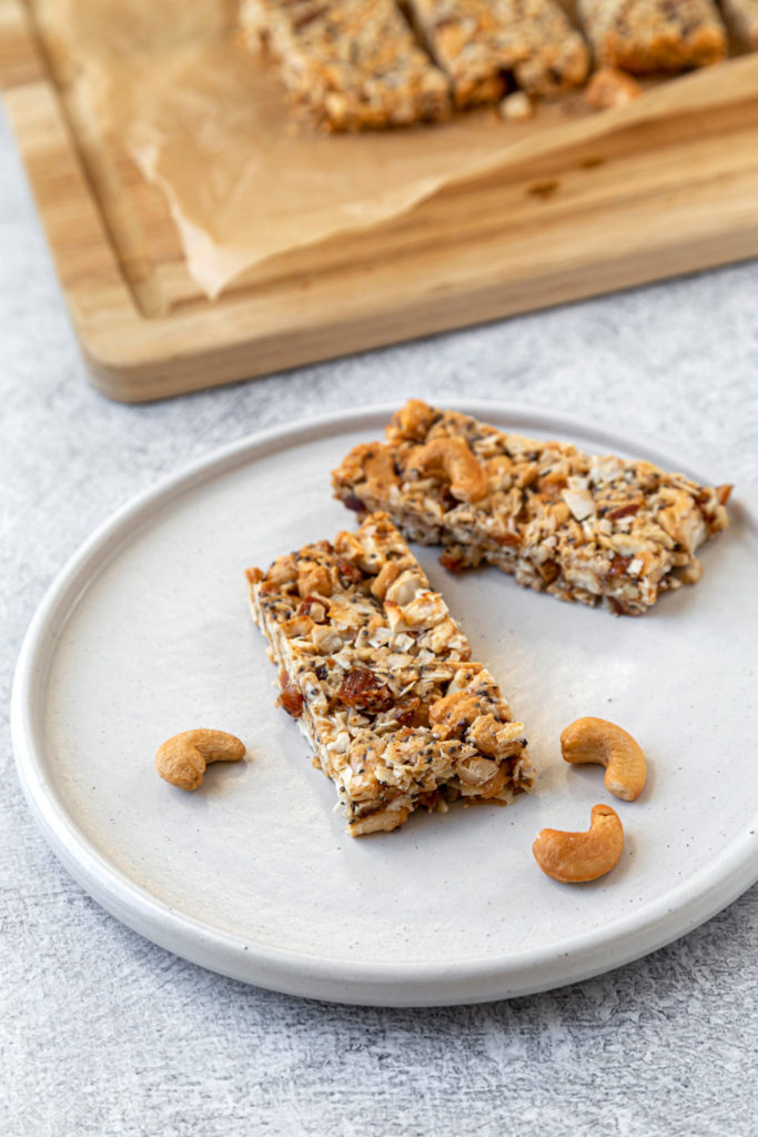 2 cashew coconut bars sitting on white plate with wooden chopping board in the background