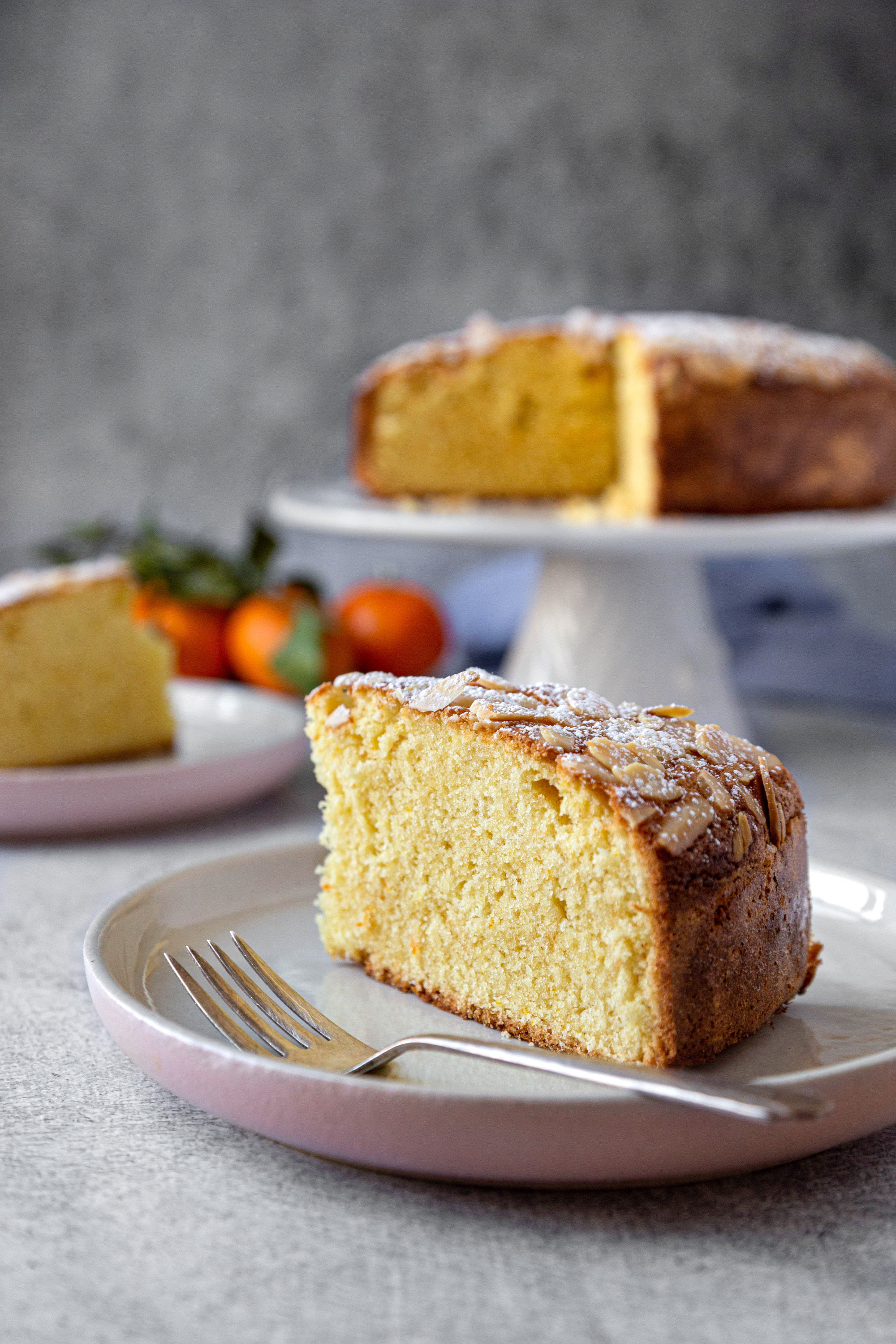 A slice of orange blossom cake on a grey plate with silver fork