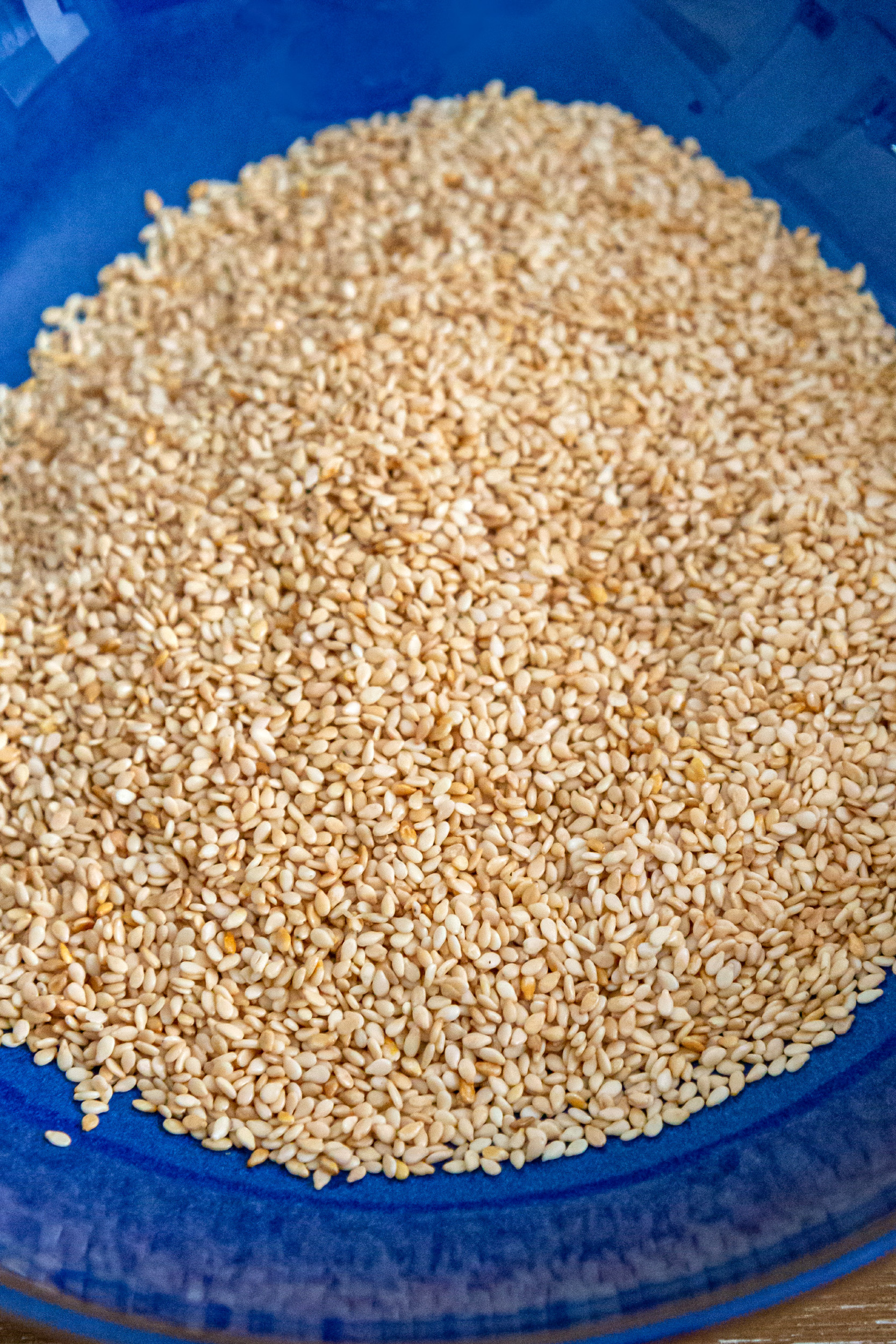 A close up of a blue bowl filled with toasted sesame seeds