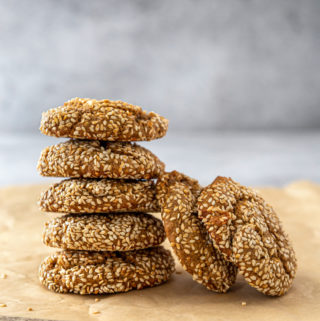 A stack of 5 sesame tahini cookies, with 2 cookies leaning against the stack on brown parchment paper