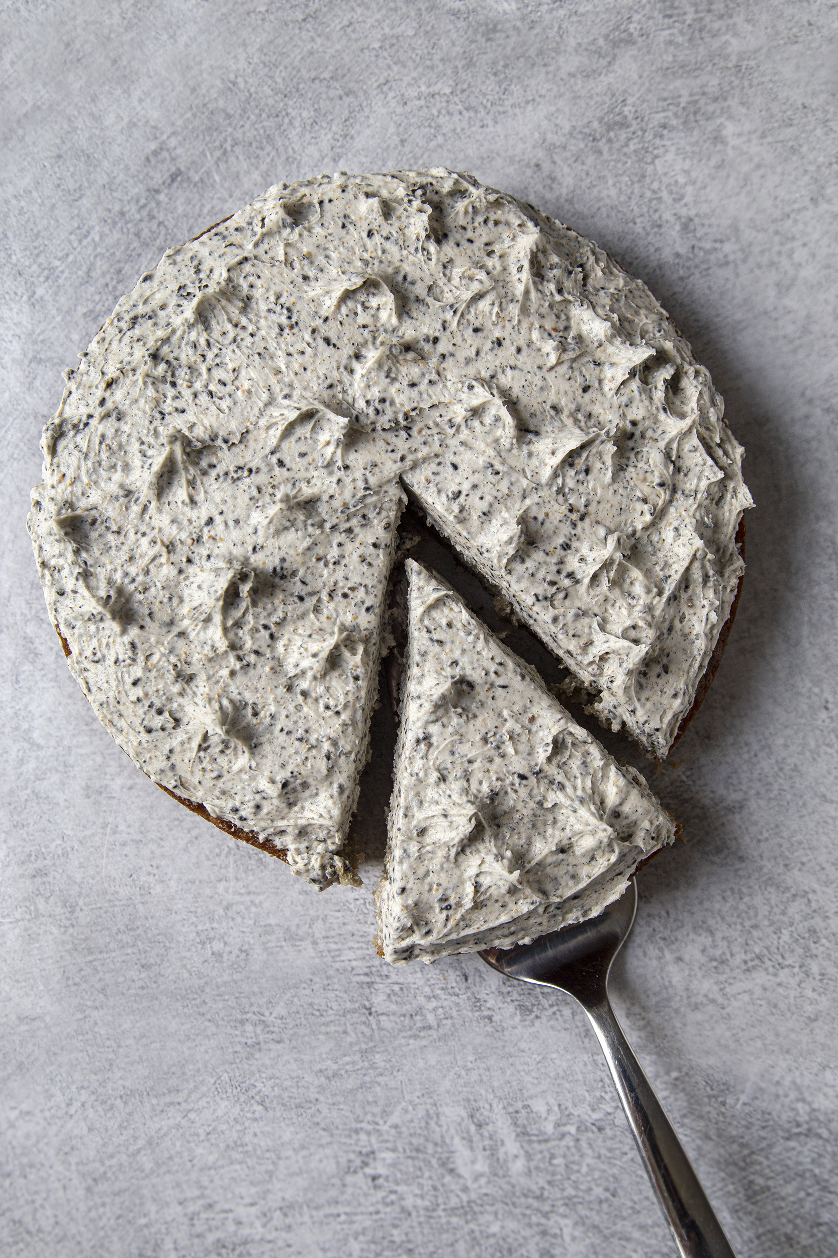 Bird's eye view of black sesame cake, shown on grey background, with a cake slice cut