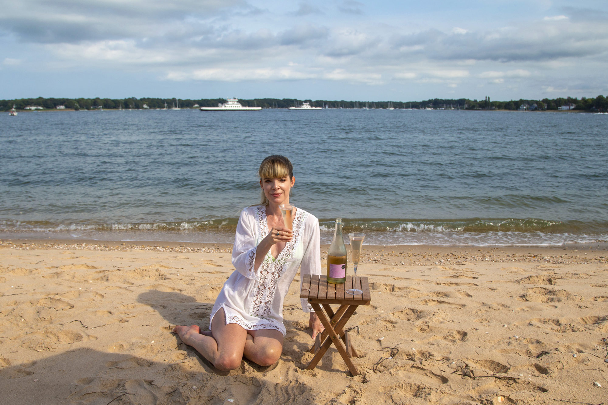A woman sitting on the sand holding a flute of sparkling wine 
