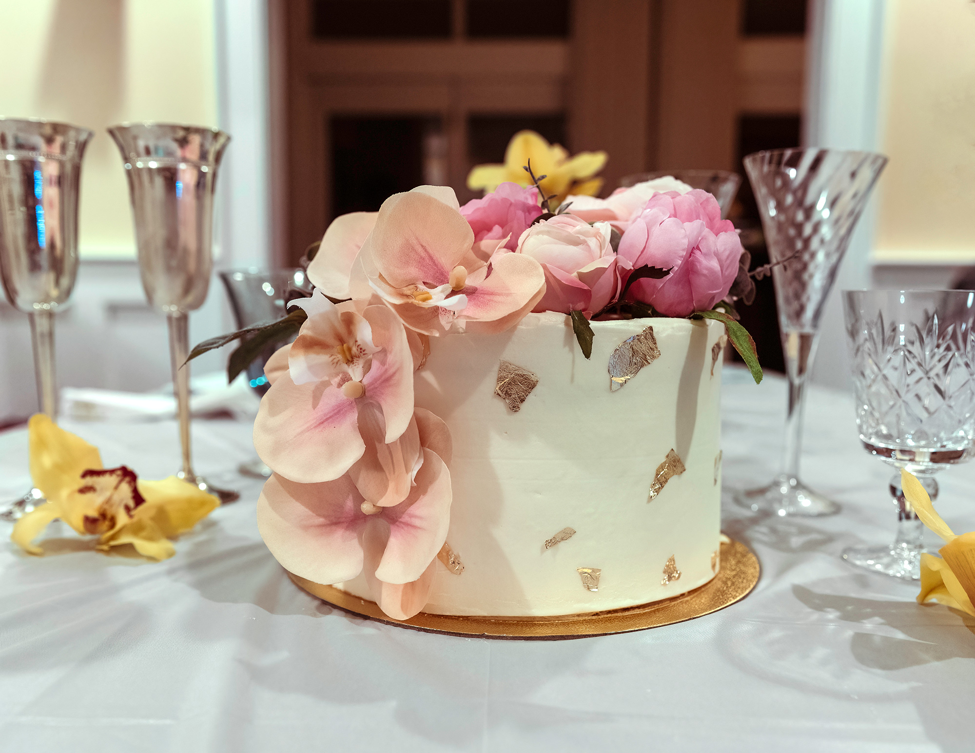 A wedding cake with edible gold leaf, vanilla frosting and pink orchids cascading down the side.